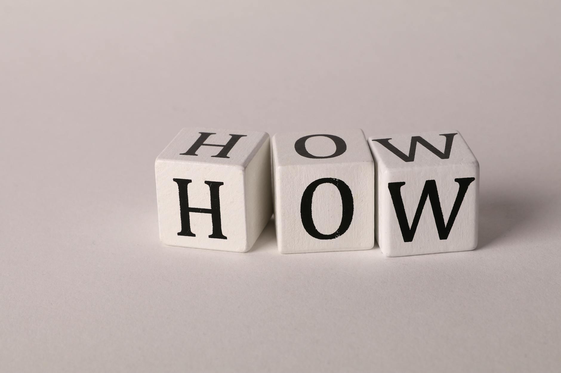 Close-up of white wooden cubes with the letters 'H', 'O', and 'W' arranged on a neutral background.